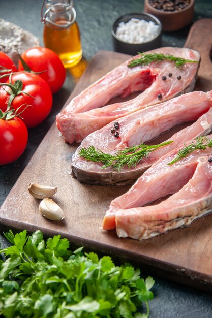 Vue de face des tranches de poisson frais avec des tomates et des verts sur la surface sombre des aliments santé salade de repas de couleur poivre de fruits de mer de l'eau de mer