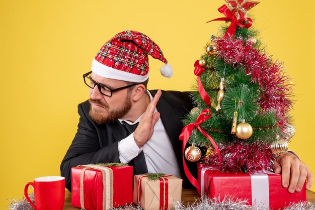 Vue de face travailleur masculin assis derrière son lieu de travail avec des cadeaux sur jaune