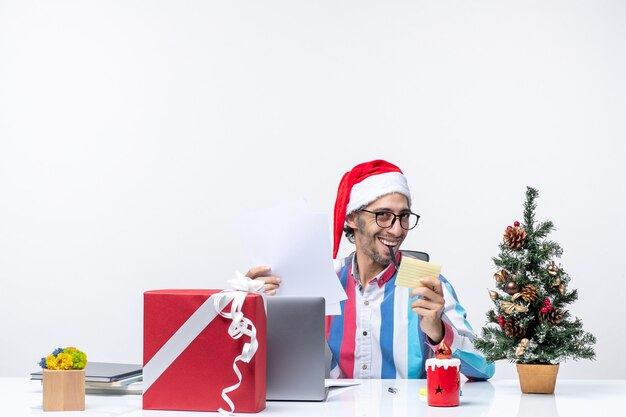 Vue de face travailleur masculin assis à sa place avec un ordinateur portable écrit des notes de bureau d'émotion d'emploi Noël