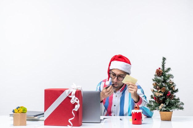 Vue de face travailleur masculin assis à sa place avec un ordinateur portable écrit des notes émotion travail de bureau Noël