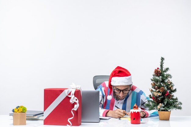 Vue de face travailleur masculin assis à sa place avec un ordinateur portable écrit des notes émotions bureau travail de Noël