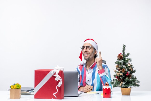 Vue de face travailleur masculin assis à sa place avec un ordinateur portable et des fichiers écrivant des notes bureau de vacances de Noël