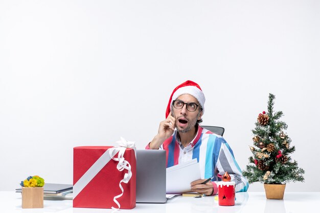 Vue de face travailleur masculin assis à sa place avec un ordinateur portable travaillant avec des documents émotions de bureau de travail de Noël