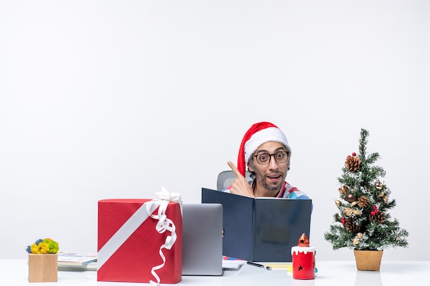 Vue de face travailleur masculin assis sur son lieu de travail lecture cahier d'affaires émotions emploi bureau de noël