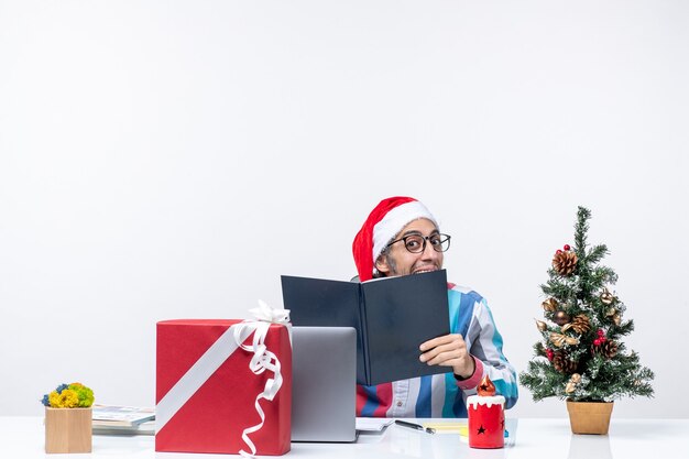 Vue de face travailleur masculin assis sur son lieu de travail tenant un cahier d'affaires bureau de noël