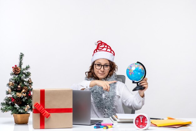 Vue de face une travailleuse assise devant son lieu de travail tenant un petit globe emploi entreprise travail bureau noël