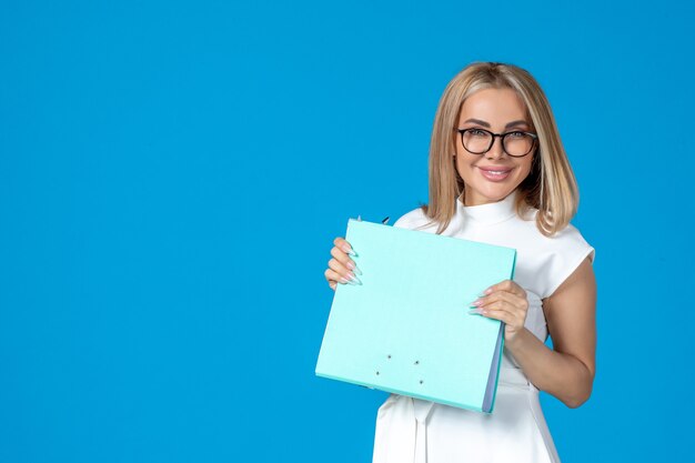 Vue de face d'une travailleuse en robe blanche tenant un dossier sur un mur bleu