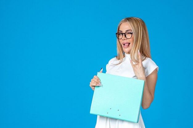Vue de face d'une travailleuse en robe blanche tenant un dossier sur un mur bleu