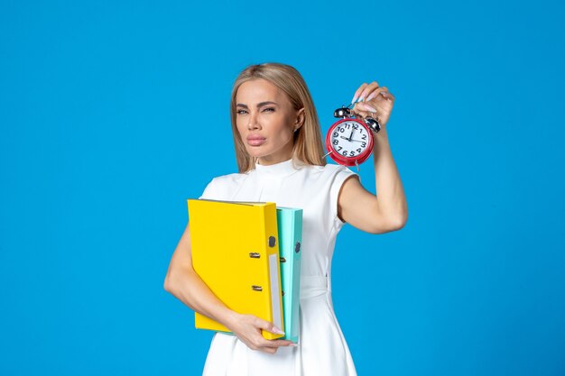 Vue de face d'une travailleuse tenant un dossier et une horloge sur le mur bleu