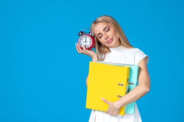 Vue de face d'une travailleuse tenant un dossier et une horloge sur le mur bleu