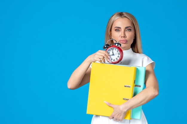 Vue de face d'une travailleuse tenant un dossier et une horloge sur le mur bleu