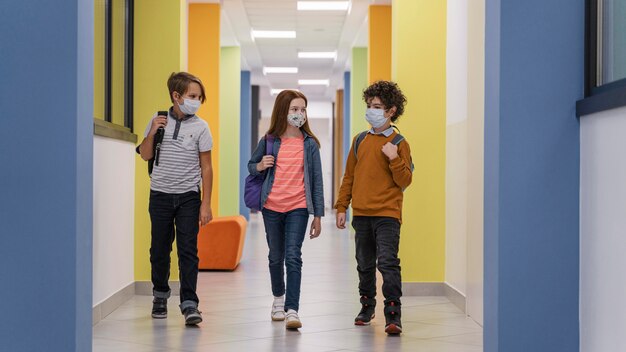 Vue de face de trois enfants sur le couloir de l'école avec des masques médicaux