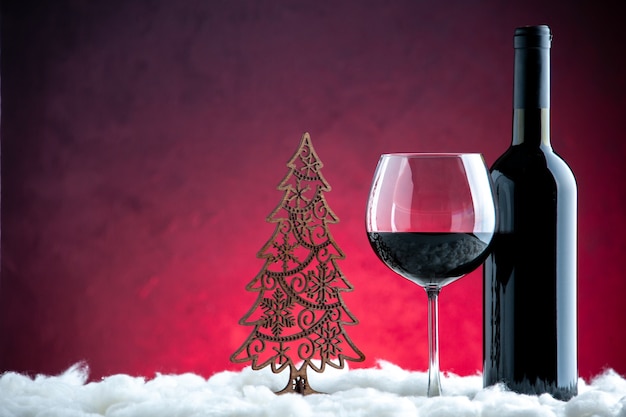 Vue de face un verre de vin bouteille de vin décoration de Noël sur fond rouge foncé