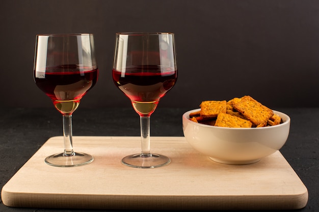 Une vue de face verres de vin avec chips à l'intérieur de la plaque sur un bureau en bois et sombre