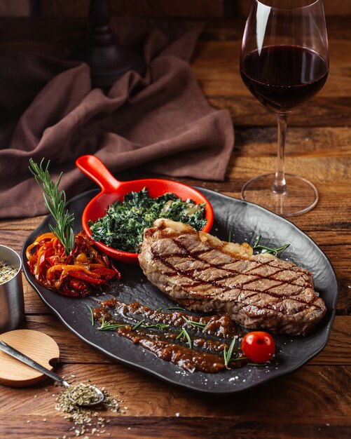 Une vue de face de la viande frite avec des verts à l'intérieur de la plaque sombre sur le dîner de repas de bureau en bois brun