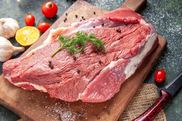 Vue de face de la viande rouge crue fraîche sur une planche à découper en bois sur une serviette de couleur nude à l'ail citronné sur fond de couleur mélangée