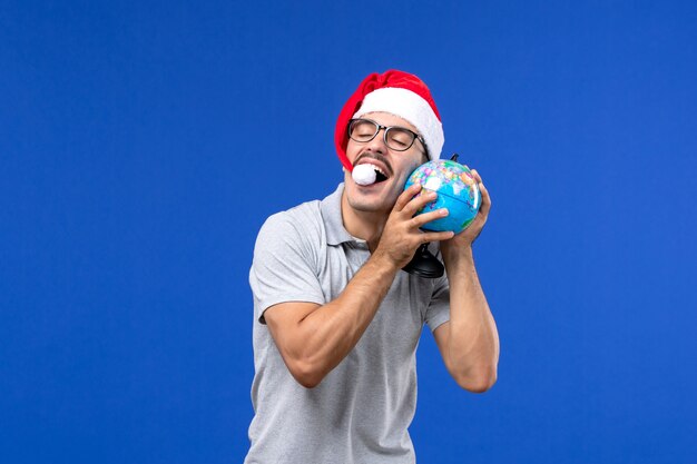 Vue de face young male holding globe terrestre sur mur bleu voyage avion vacances mâle