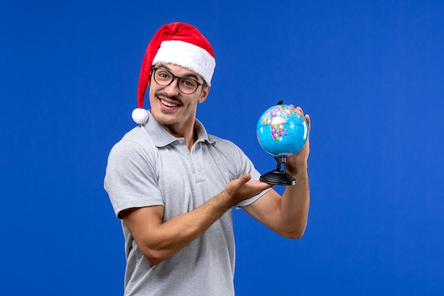 Vue de face young male holding globe terrestre sur le mur bleu voyage avions humains vacances