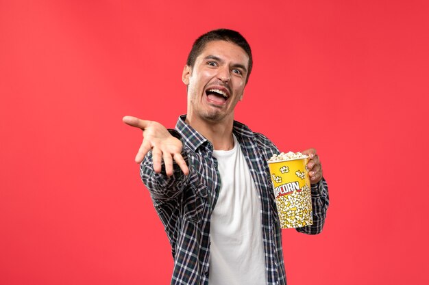 Vue de face young male holding pop-corn avec une expression inquiétante sur le mur rouge clair cinéma films cinéma mâle