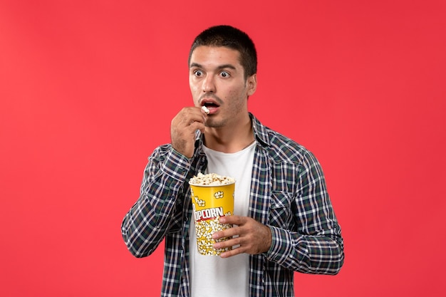 Vue de face young male holding pop-corn et manger sur le mur rouge clair mâle cinéma cinéma film