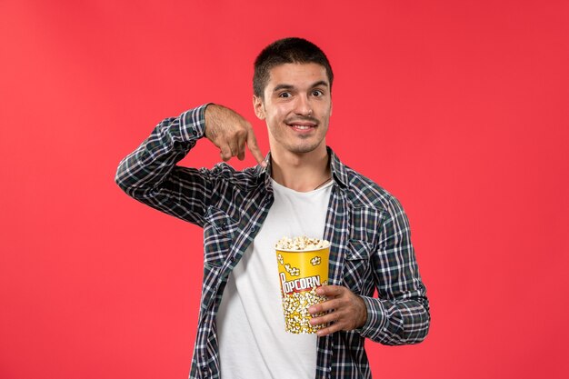 Vue de face young male holding pop-corn sur mur rouge clair mâle films cinéma cinéma film