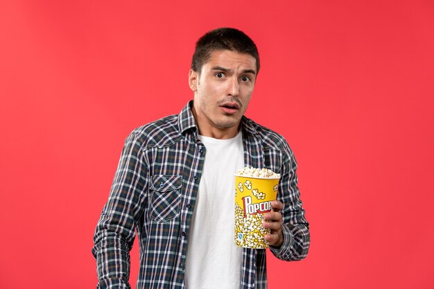Vue de face young male holding pop-corn package sur le mur rouge clair cinéma cinéma film mâle film