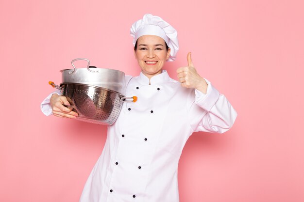 A, vue frontale, jeune femme, cuisinier, dans, cuisinier blanc, complet, blanc, casquette, poser, tenue, argent, casseroles, sourire