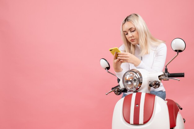 Vue frontale, jeune femme, sur, cyclomoteur, regarder, téléphone