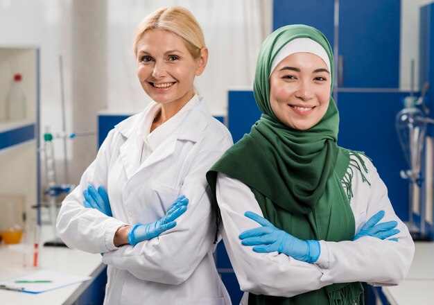 Vue frontale, de, smiley, femmes scientifiques, dans, les, laboratoire, poser, à, bras croisés