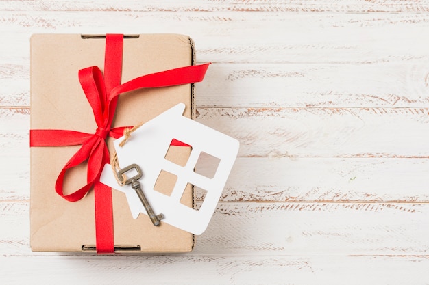 Photo gratuite vue grand angle d'une boîte-cadeau attachée avec un ruban rouge sur la clé de la maison sur une table en bois