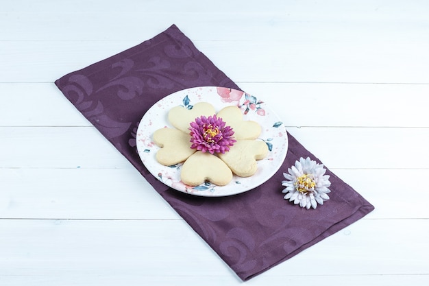 Photo gratuite vue grand angle de cookies en forme de coeur, fleurs sur napperon sur fond de planche de bois blanc. horizontal