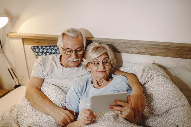 Vue grand angle d'un couple de personnes âgées utilisant un pavé tactile tout en se reposant dans la chambre