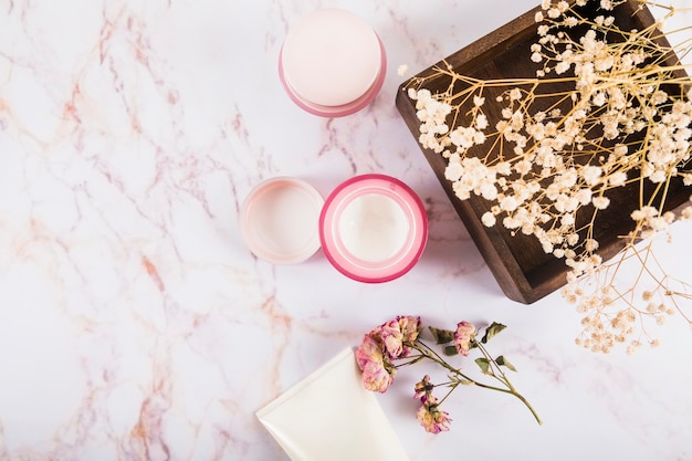 Photo gratuite vue grand angle de crème nourrissante et de fleurs sur marbre