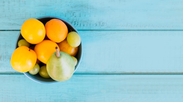 Vue grand angle de divers fruits juteux dans un bol sur le dessus de table en bois bleu