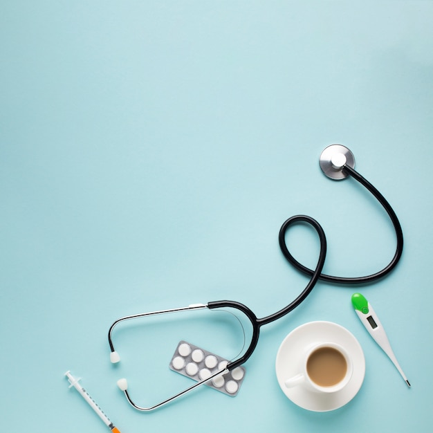 Vue grand angle du stéthoscope; tasse à café; comprimés; thermomètre; injection sur le bureau bleu