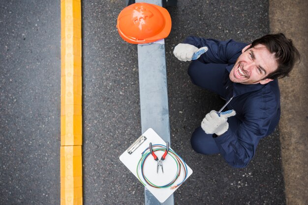 Vue grand angle d&#39;électricien mâle heureux, montrant le pouce vers le haut au lieu de travail