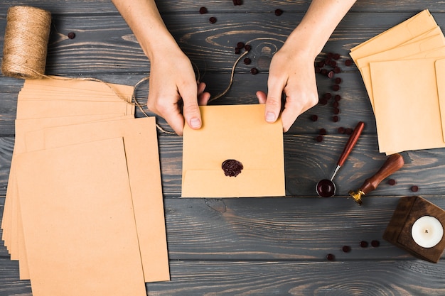 Vue grand angle de femme montrant le phoque sur une enveloppe brune avec du matériel d&#39;artisanat sur une table en bois