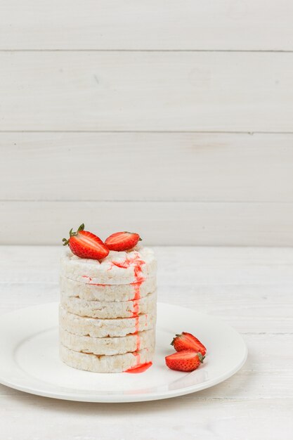 Vue grand angle des gâteaux de riz blanc sur plaque avec des fraises sur la surface de la planche de bois blanc. espace libre vertical pour votre texte