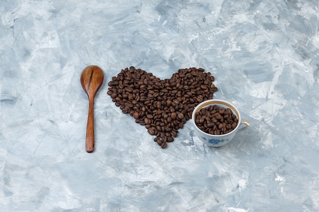 Vue grand angle des grains de café dans une tasse avec une cuillère en bois sur fond de plâtre gris. horizontal