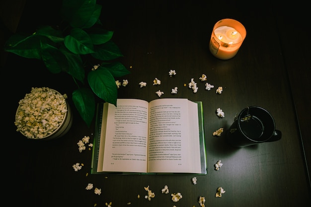 Photo gratuite vue grand angle d'un livre ouvert et du maïs soufflé sur la table avec une bougie allumée et une tasse de thé