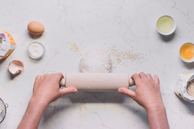 Vue grand angle de la main d&#39;une personne aplatissant la pâte avec un rouleau à pâtisserie