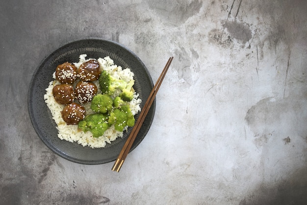 Vue grand angle de riz cuit avec des boulettes de viande et du brocoli dans une assiette sur la table avec des baguettes