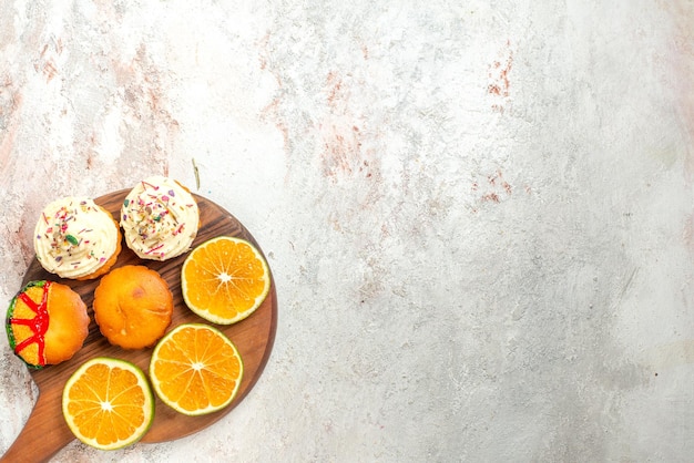 Vue en gros plan de dessus des biscuits appétissants et des tranches d'orange sur la planche à découper sur le côté gauche de la table