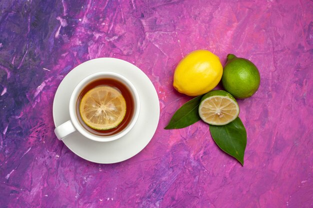 Vue en gros plan de dessus une tasse de citron vert et de thé avec des feuilles à côté de la tasse de thé savoureux au citron sur la table rose-violet