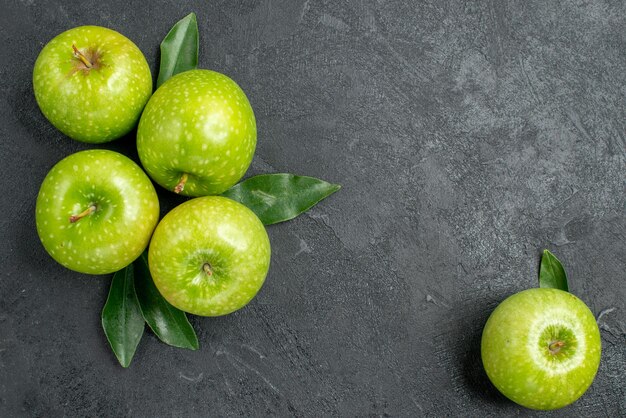 Vue en gros plan des pommes quatre pommes vertes avec des feuilles à côté de la pomme sur la table sombre