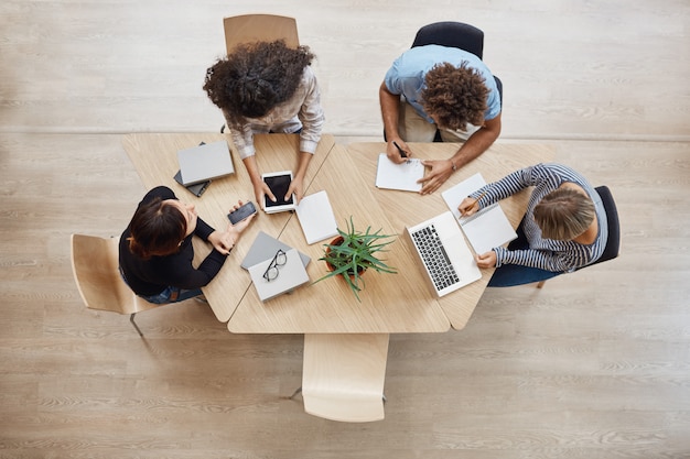 Vue d'en-haut. Entreprise, démarrage, concept de travail d'équipe. Des partenaires de démarrage assis dans un espace de coworking parlent d'un futur projet, examinant des exemples de travail sur un ordinateur portable et une tablette numérique.