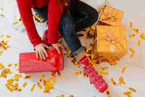 Photo gratuite vue d'en haut sur la femme en chaussettes rouges assis à la maison à noël sur des confettis dorés déballage peresents et coffrets cadeaux