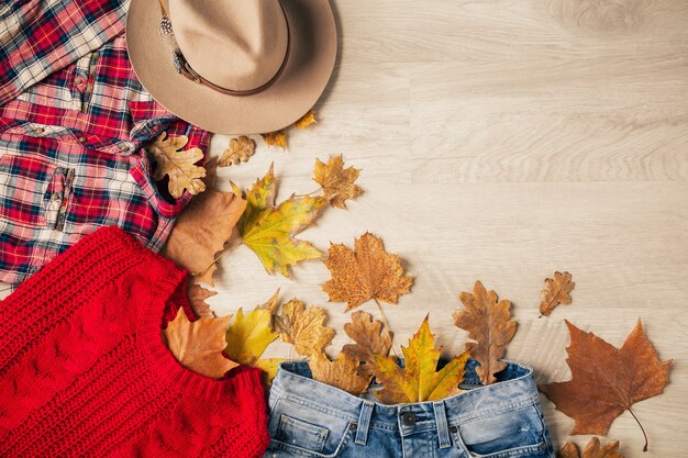 Vue d'en haut sur la mise à plat du style femme et accessoires, pull en tricot rouge, chemise en flanelle à carreaux, jeans en denim, chapeau, tendance de la mode automne, vue d'en haut, vêtements, feuilles jaunes