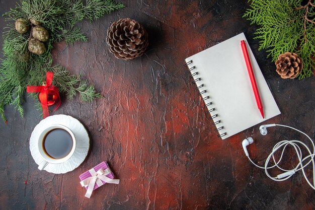 Vue horizontale des branches de sapin une tasse d'accessoires de décoration de thé noir casque blanc et cadeau à côté d'un ordinateur portable avec un stylo sur fond sombre