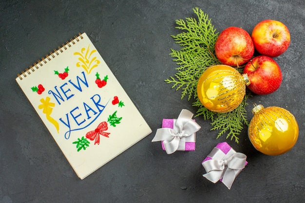 Vue horizontale des cadeaux et des pommes fraîches biologiques naturelles et des accessoires de décoration avec inscription du nouvel an sur fond noir